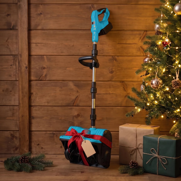 An orange-and-black snow shovel with its shaft folded, wrapped in a loose red ribbon and a plain bow around its head and leaning against a wooden wall beside a lit Christmas tree, a blank kraft tag on the ribbon and wrapped boxes on the floor